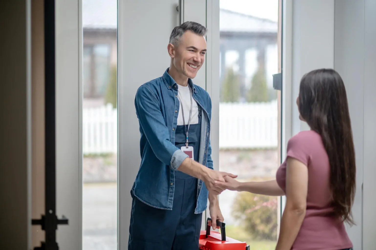 HVAC technician being greeted by homeowner shaking hands at front door entrance.
