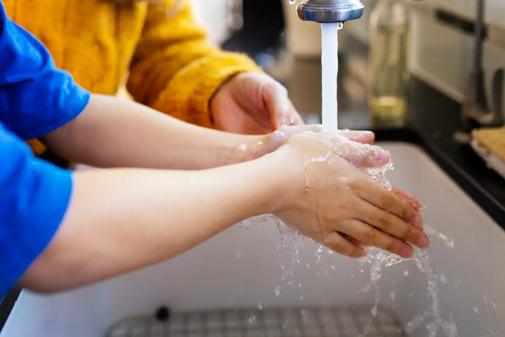 child washing hands in the sink under running water thanks to reliable water heating services.
